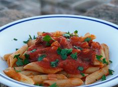 pasta with tomato sauce and parsley in a blue and white bowl on the ground