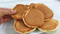 some pancakes are on a white plate and someone is holding the pancake in their hand