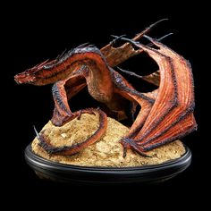 a red dragon statue sitting on top of a pile of sand next to a black background