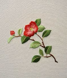 a red flower with green leaves is on a white surface, and it appears to be embroidered onto the fabric