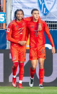 two soccer players in red uniforms are walking on the field with their arms around each other