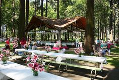 tables and benches are set up in the woods for an outdoor wedding reception with white tablecloths and pink flowers