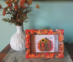 a vase filled with flowers next to a picture frame on top of a wooden table