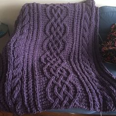 a purple knitted blanket sitting on top of a blue couch next to a pillow