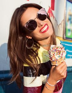 a woman wearing sunglasses and holding a donut with sprinkles on it