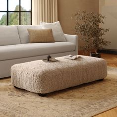 a living room with a couch, ottoman and coffee table in front of a window