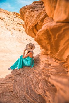 a woman wearing a hat sitting on top of a rock formation in the desert with her hands behind her head