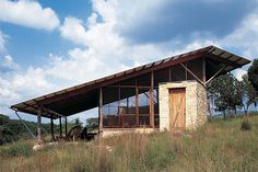 a small building sitting on top of a lush green hillside under a cloudy blue sky