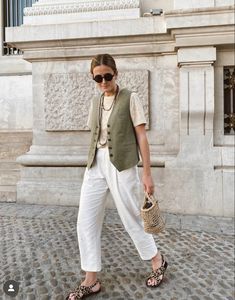 a woman is standing in front of a building wearing white pants and a green vest