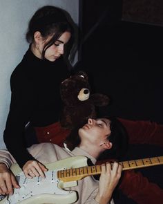 a man laying on top of a bed next to a woman holding an electric guitar