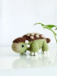 a small crocheted turtle next to a plant on a white surface with light reflection