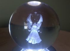 a glass ball with an angel drawn on the front and side in white ink, sitting on a wooden table