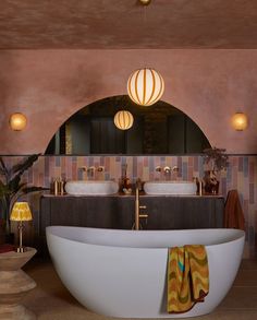 a large bath tub sitting under a mirror next to two sinks in a room with lights on the ceiling