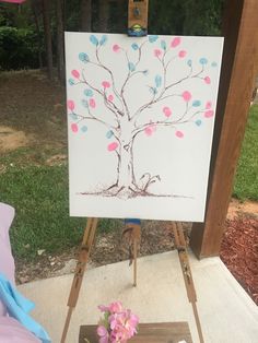 an easel with a painting on it sitting in front of a flower pot and tree