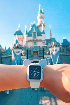 someone is holding their apple watch in front of mickey mouse's castle