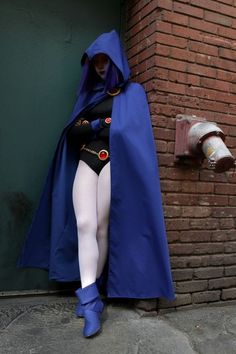 a woman in a blue cape and white tights is leaning against a brick wall