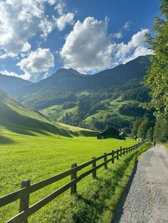 a wooden fence on the side of a dirt road next to a lush green field