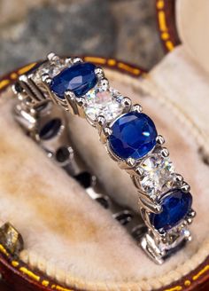 a close up of a ring with blue stones and diamonds on it in a case