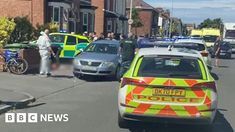 police cars parked on the side of a road with people standing around them in front of some buildings