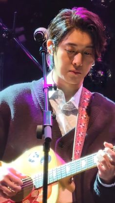 a young man playing an acoustic guitar in front of a microphone and music stand with lights behind him