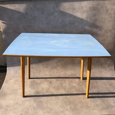 a blue table sitting on top of a cement floor next to a concrete wall and potted plant