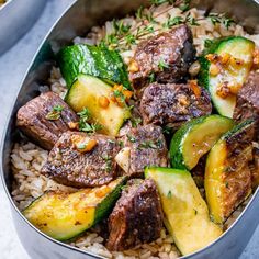 a metal bowl filled with meat and veggies on top of rice next to a fork