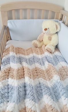 a teddy bear sitting on top of a blanket in a crib