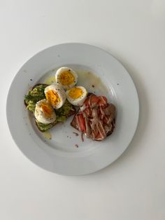 a white plate topped with eggs, bacon and broccoli on top of a table