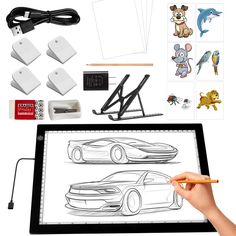 a person is holding a pencil and drawing on a tablet with various items surrounding it