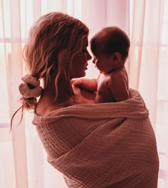 a woman is holding a baby wrapped in a blanket while she looks out the window