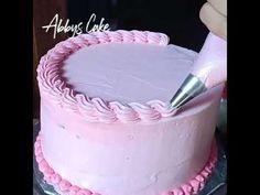 a cake with pink frosting and a hand holding a knife