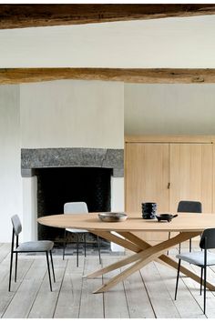 a wooden table with chairs around it in front of a fireplace