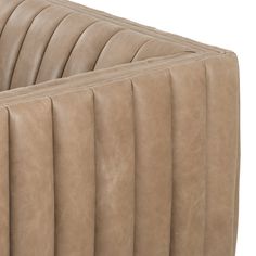 an upholstered beige leather sofa with pleated back and arms, viewed from the side