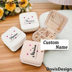 three personalized jewelry boxes sitting on top of a wooden table with flowers in the background