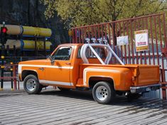 an orange pick up truck parked in front of a gated area with pipes on it