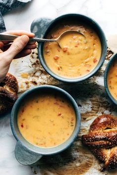 three bowls filled with soup on top of a white counter next to other dishes and bread