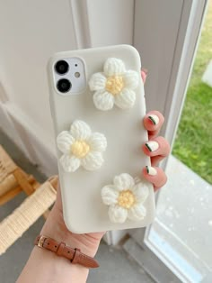 a woman holding up her phone case with crocheted flowers on it