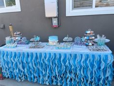 a table topped with cakes and desserts on top of blue tables clothed around it