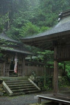 an old wooden building in the middle of a forest with stairs leading up to it