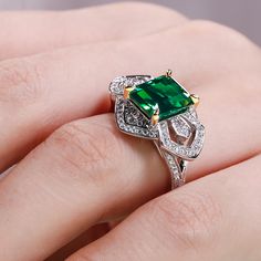 a woman's hand holding an emerald and diamond ring