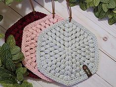 three crocheted purses hanging from hooks on a white wooden background with green leaves