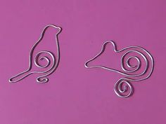 two small metal birds sitting on top of a pink surface with spirals in the middle