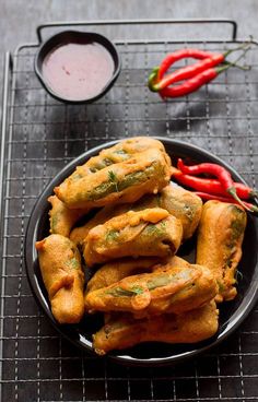 some food is on a black plate with red peppers and dipping sauce in the background