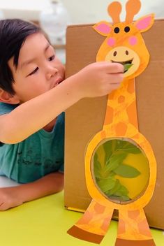 a young boy playing with a paper giraffe cut out from a cardboard box