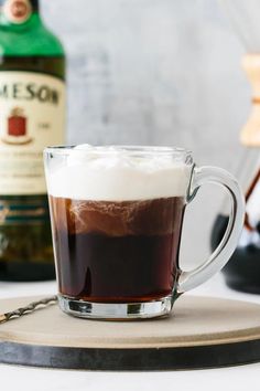 a glass mug filled with liquid sitting on top of a wooden tray next to a bottle