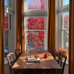 a wooden table sitting in front of two large windows with fall colored trees out the window