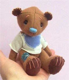 a hand holding a small brown teddy bear wearing a blue bib and white shirt