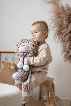 a small child sitting on a stool holding a stuffed animal