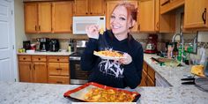 a woman is holding up some food in her hands while standing at the kitchen counter