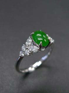 a close up of a ring with green stones and diamonds on the bottom, sitting on a gray surface